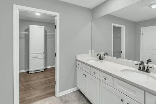 bathroom featuring wood finished floors, a sink, baseboards, and double vanity