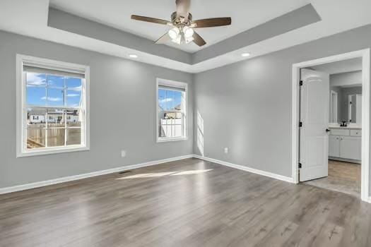 empty room with ceiling fan, baseboards, a raised ceiling, and wood finished floors