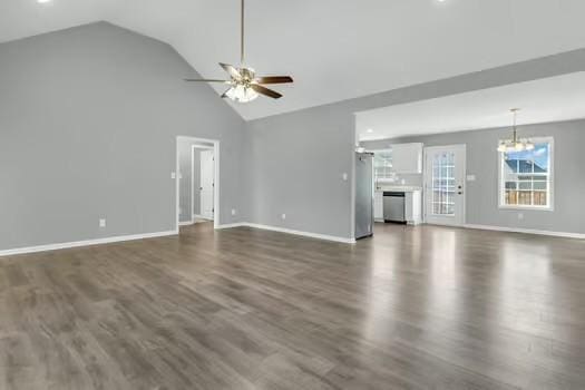 unfurnished living room with ceiling fan with notable chandelier, high vaulted ceiling, dark wood-type flooring, and baseboards