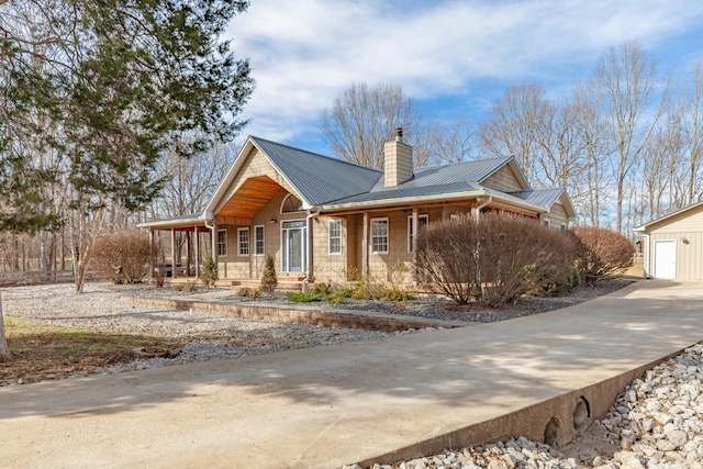 view of front of house with driveway, a chimney, metal roof, an outdoor structure, and a porch