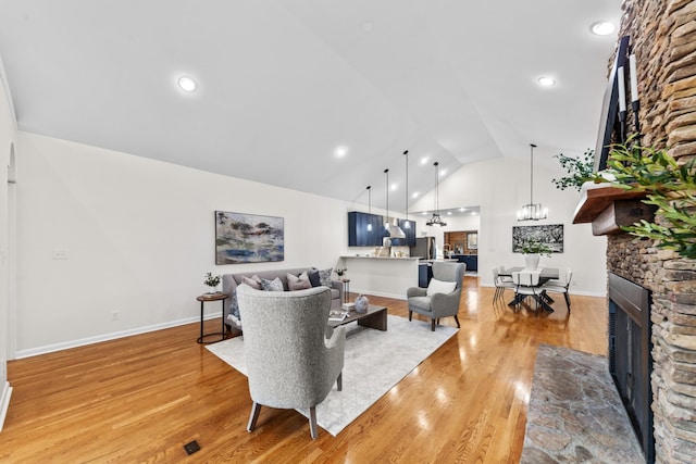 living area with high vaulted ceiling, light wood-type flooring, a stone fireplace, and an inviting chandelier