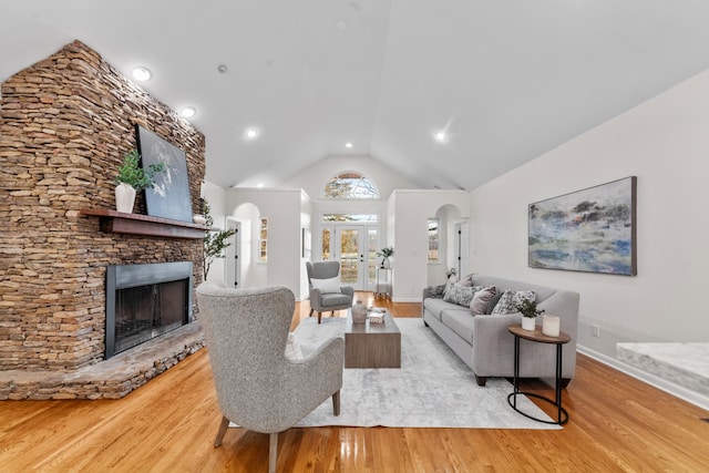 living room featuring arched walkways, a stone fireplace, and wood finished floors