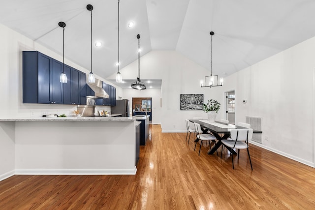 kitchen with visible vents, wood finished floors, freestanding refrigerator, blue cabinets, and wall chimney range hood