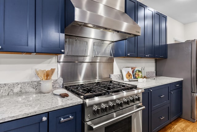 kitchen with stainless steel appliances, wall chimney range hood, light wood-style floors, and blue cabinets