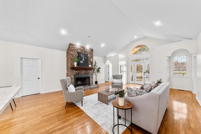 living area with light wood-style floors, arched walkways, vaulted ceiling, and a stone fireplace