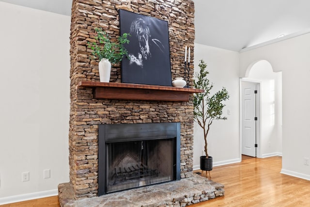 interior details featuring arched walkways, a fireplace, baseboards, and wood finished floors