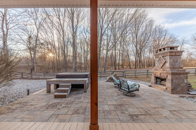 view of patio with an outdoor stone fireplace, fence, and a hot tub