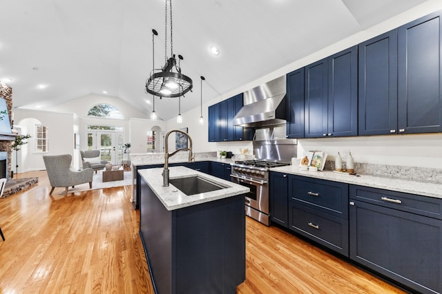 kitchen with a fireplace, light wood finished floors, stainless steel stove, a sink, and wall chimney exhaust hood