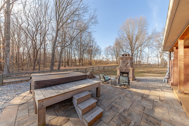 view of patio featuring a hot tub, fence, and an outdoor stone fireplace