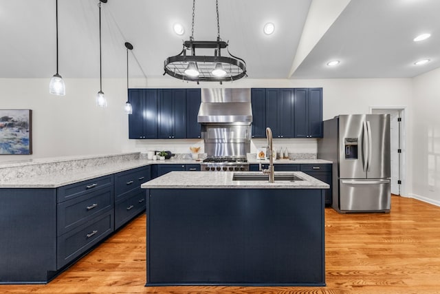 kitchen featuring blue cabinetry, a sink, wall chimney range hood, light wood-type flooring, and stainless steel fridge