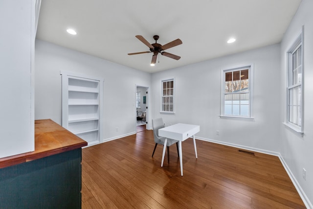 home office featuring built in features, visible vents, hardwood / wood-style floors, ceiling fan, and baseboards