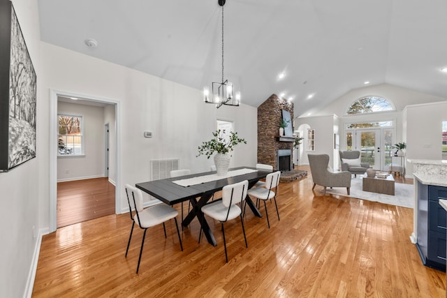 dining space with vaulted ceiling, a stone fireplace, plenty of natural light, and light wood-style flooring