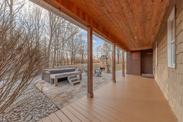 wooden terrace with a hot tub, an outdoor stone fireplace, and a patio