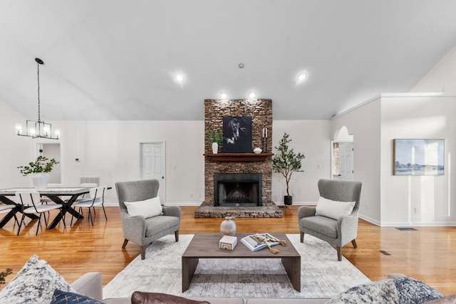 living room with baseboards, lofted ceiling, light wood-style floors, a fireplace, and a chandelier