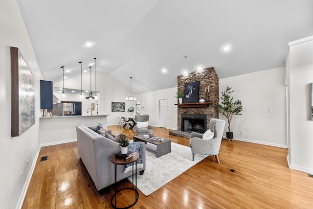 living area featuring light wood finished floors, visible vents, vaulted ceiling, a stone fireplace, and baseboards