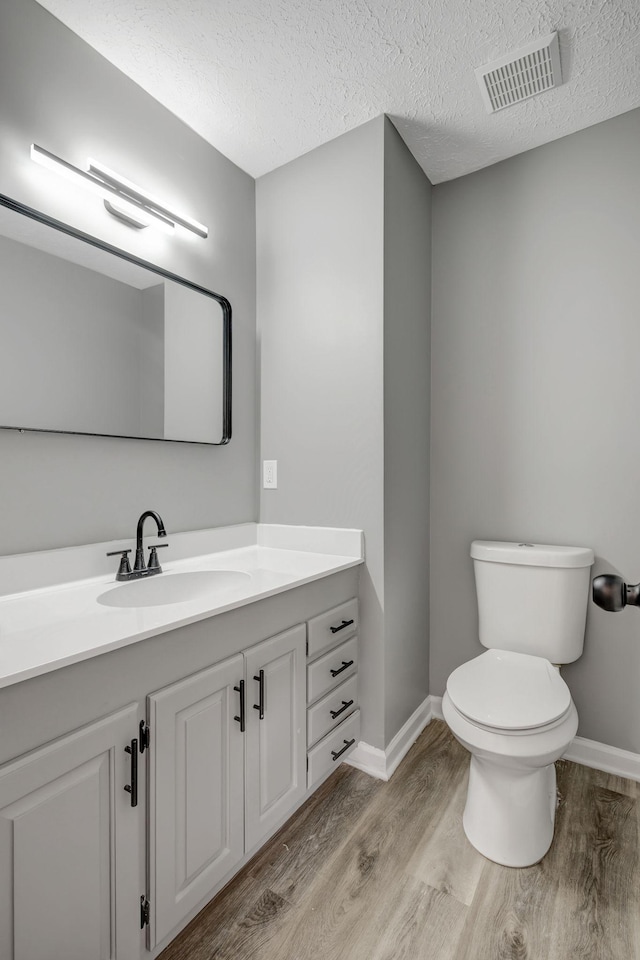 bathroom with visible vents, toilet, wood finished floors, a textured ceiling, and vanity