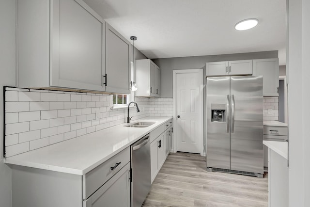 kitchen featuring stainless steel appliances, light countertops, backsplash, light wood-style floors, and a sink