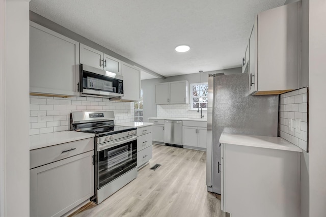 kitchen with tasteful backsplash, light countertops, hanging light fixtures, light wood-style flooring, and appliances with stainless steel finishes