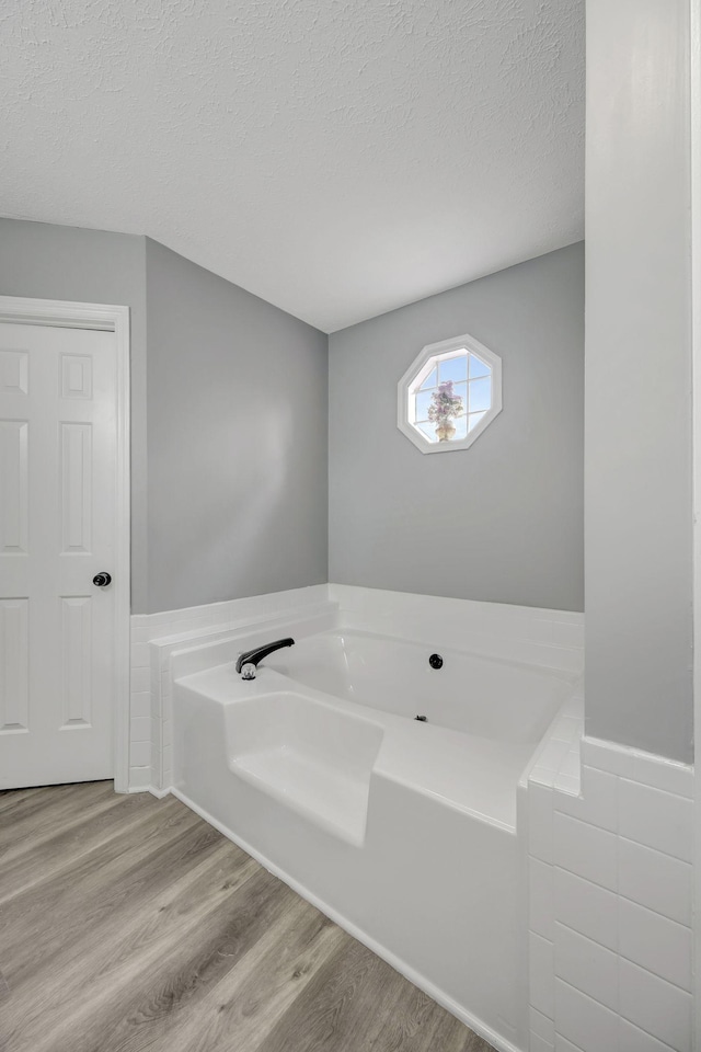 bathroom featuring a textured ceiling, a bath, and wood finished floors