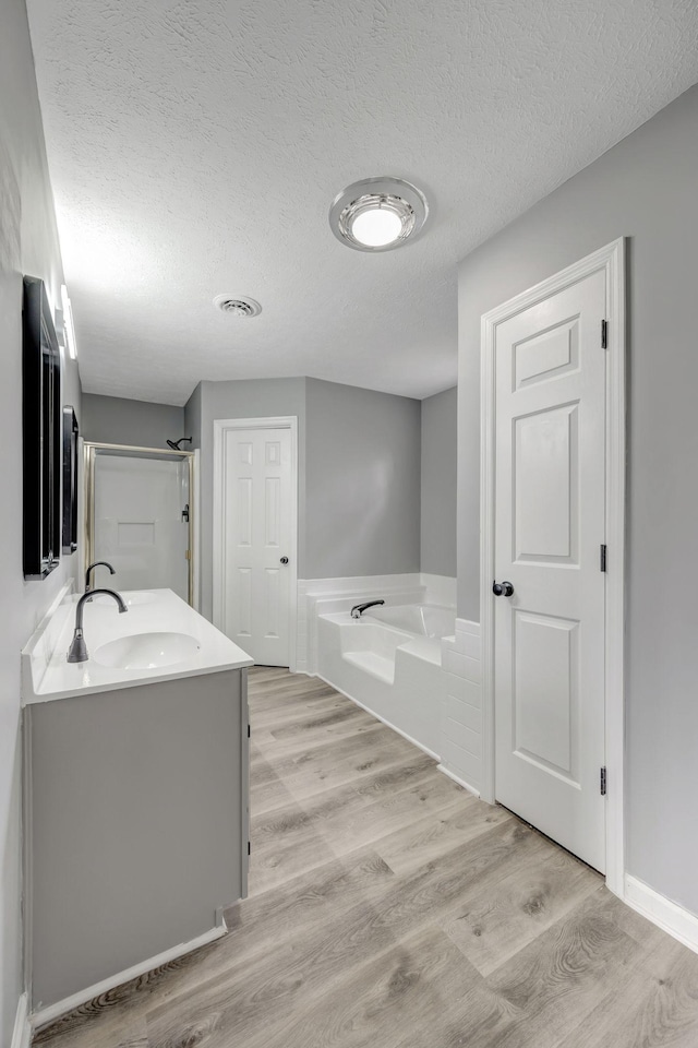 full bathroom with double vanity, wood finished floors, a sink, a textured ceiling, and a bath