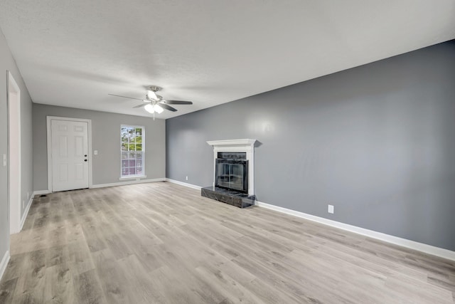 unfurnished living room with light wood finished floors, ceiling fan, a premium fireplace, and baseboards