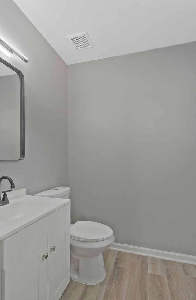 bathroom with visible vents, toilet, vanity, wood finished floors, and baseboards