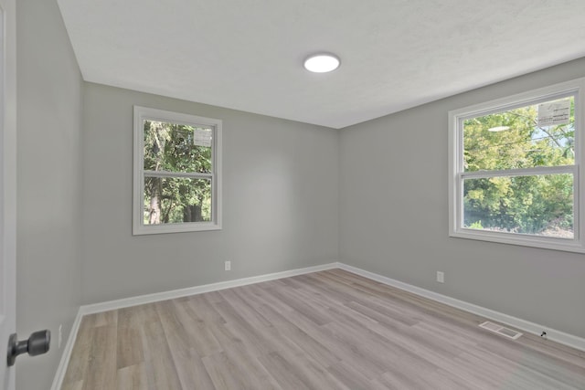 unfurnished room with a wealth of natural light, visible vents, light wood finished floors, and baseboards