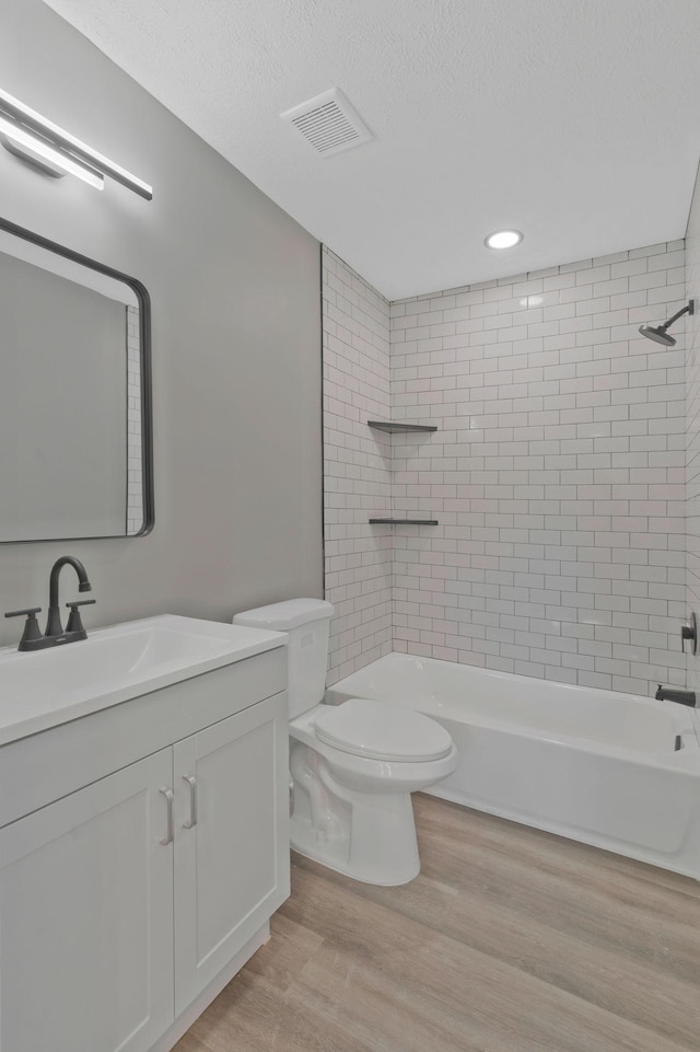 full bath with a textured ceiling, toilet, wood finished floors, vanity, and visible vents