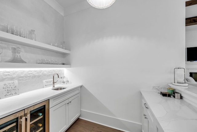 bar featuring dark wood-style floors, indoor wet bar, decorative backsplash, a sink, and baseboards