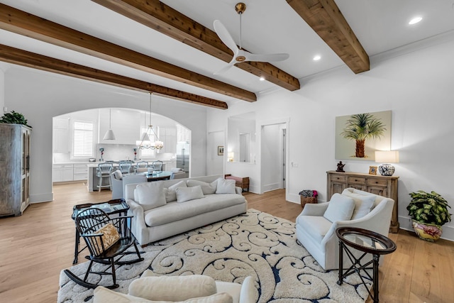 living room with arched walkways, beamed ceiling, light wood-style flooring, and ceiling fan with notable chandelier