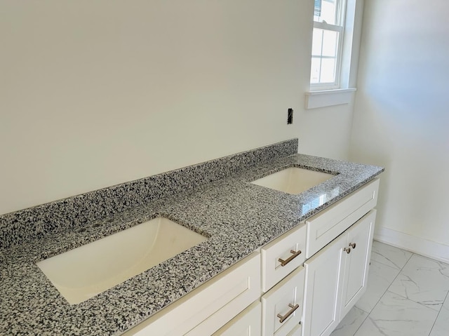 bathroom with marble finish floor, double vanity, a sink, and baseboards