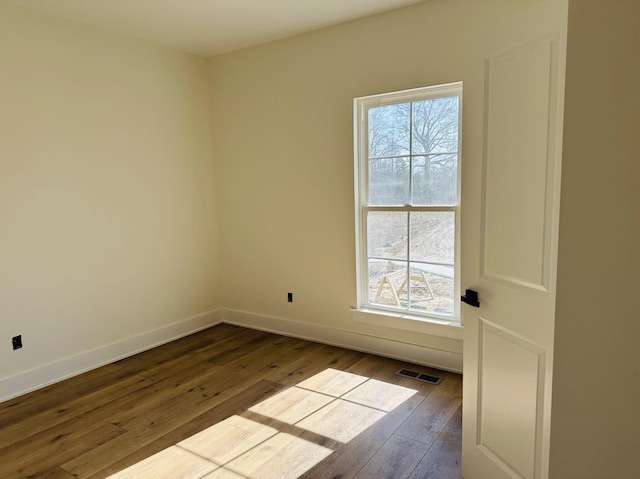 unfurnished room with baseboards, dark wood finished floors, visible vents, and a healthy amount of sunlight