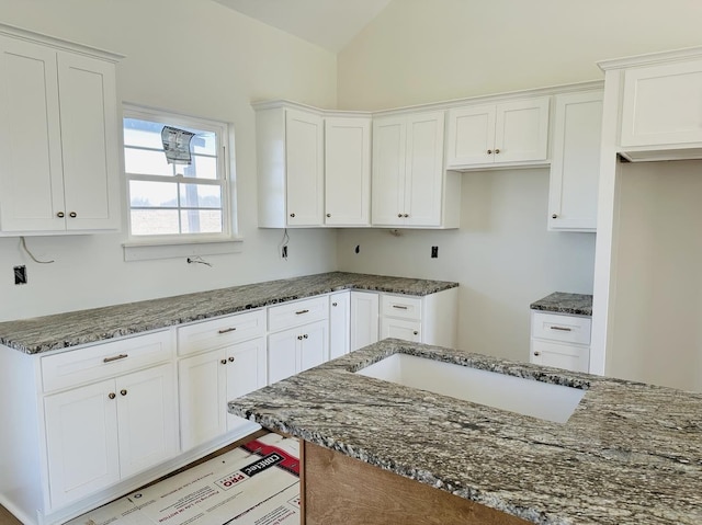 kitchen featuring white cabinetry, vaulted ceiling, and dark stone countertops