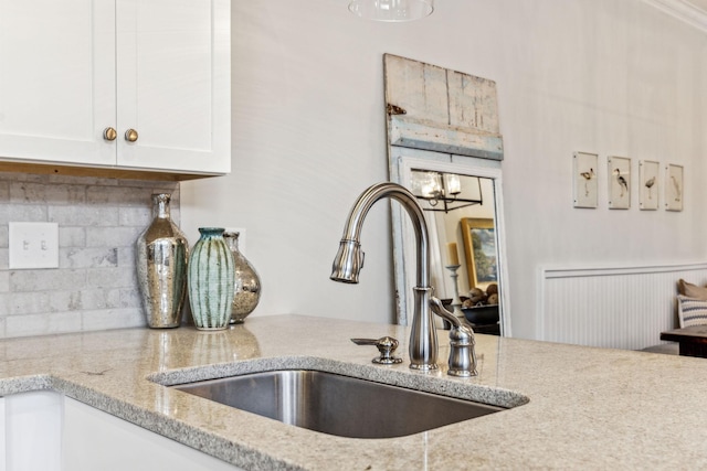 kitchen with backsplash, light stone counters, white cabinets, and a sink