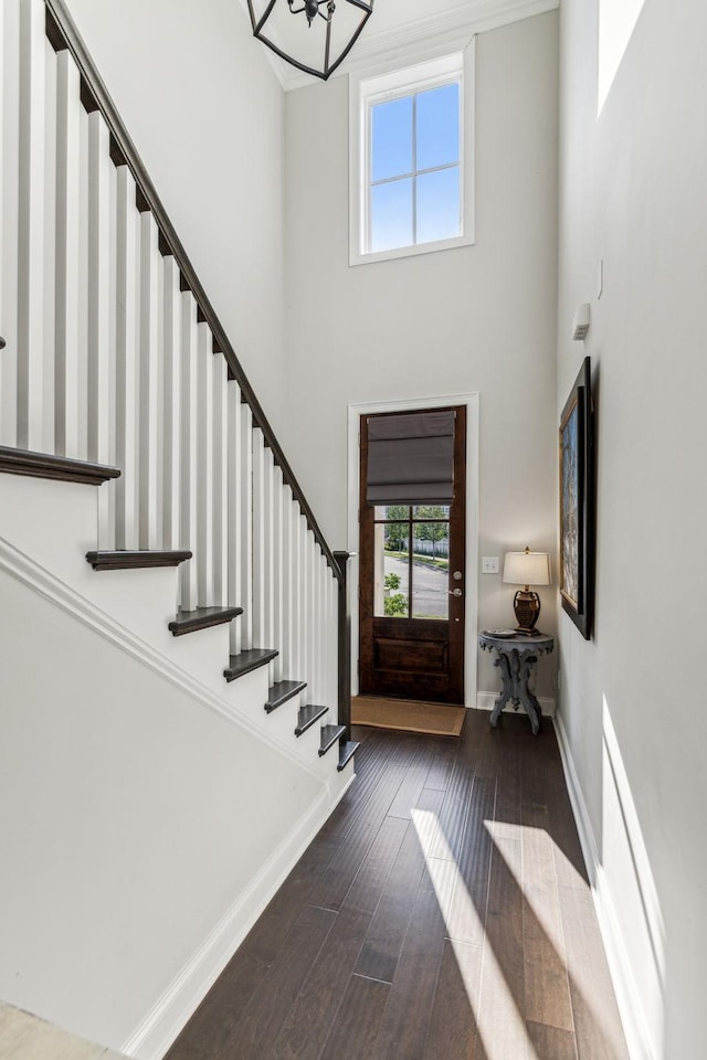 entrance foyer with dark wood-style floors, stairs, a towering ceiling, and baseboards