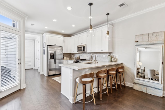 kitchen with a peninsula, a sink, white cabinets, hanging light fixtures, and appliances with stainless steel finishes