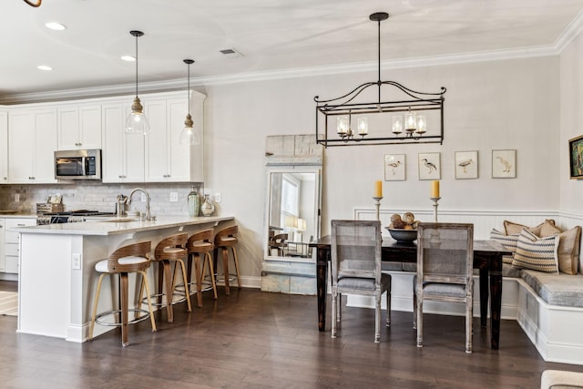 kitchen featuring a peninsula, stainless steel microwave, white cabinets, and pendant lighting