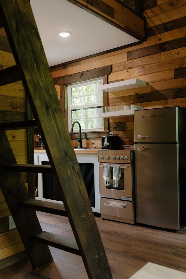 kitchen with stainless steel appliances, wood walls, a sink, and wood finished floors