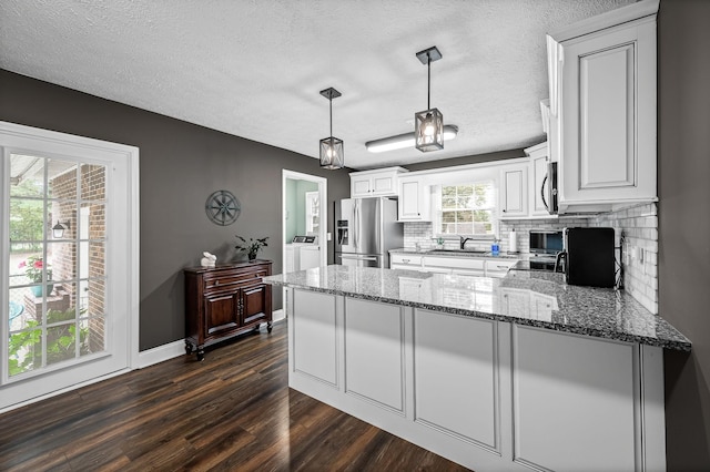 kitchen with light stone counters, a peninsula, stainless steel appliances, washer and dryer, and a sink