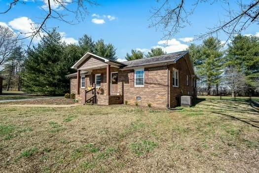 view of front facade featuring crawl space, brick siding, central AC, and a front lawn