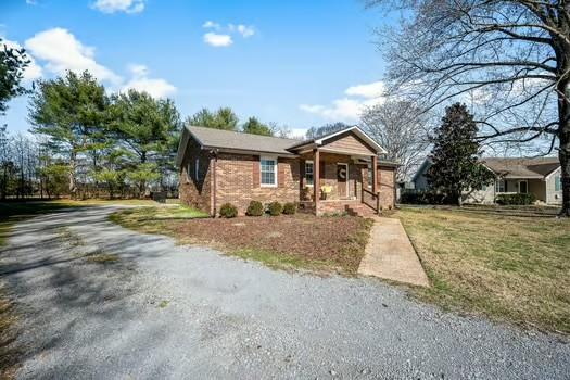 view of front of property with covered porch, a front lawn, gravel driveway, and brick siding