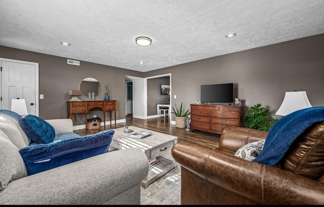 living room featuring baseboards, a textured ceiling, visible vents, and wood finished floors