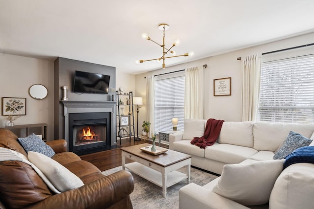 living room featuring a notable chandelier, wood finished floors, and a glass covered fireplace