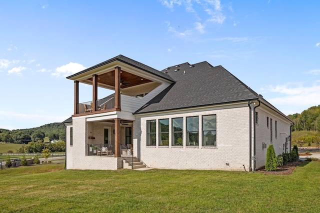 rear view of house with a ceiling fan, a yard, and a balcony