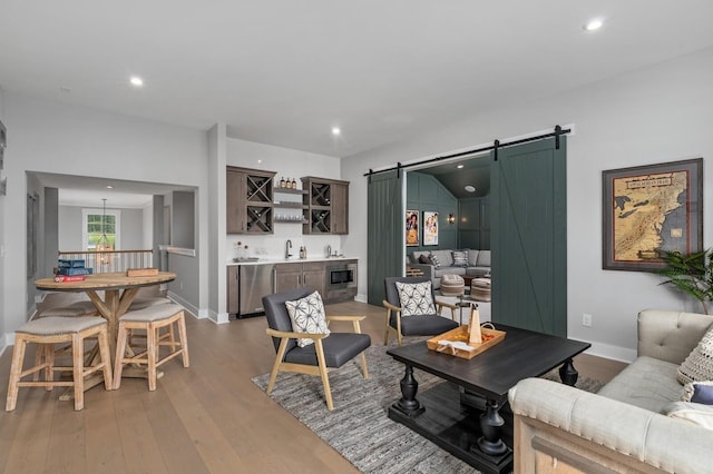 living area with light wood-type flooring, a barn door, indoor wet bar, and recessed lighting