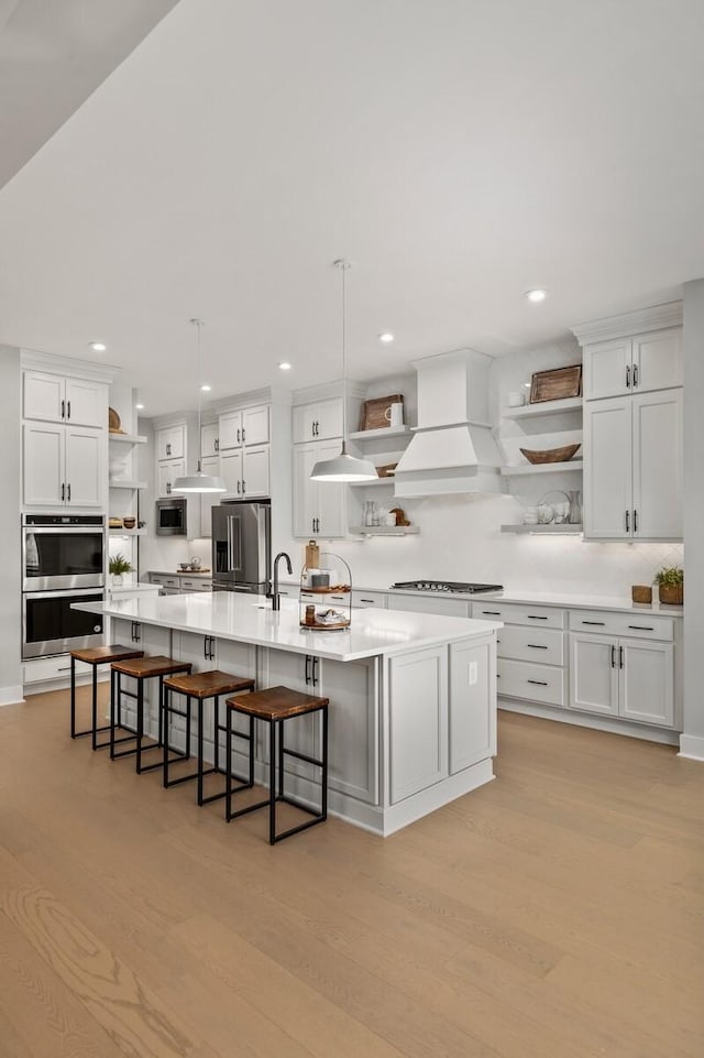 kitchen featuring light countertops, appliances with stainless steel finishes, custom exhaust hood, open shelves, and light wood finished floors