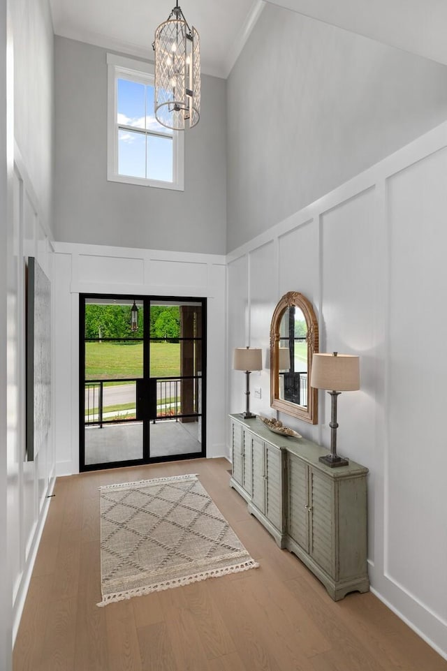 foyer with light wood finished floors, a towering ceiling, crown molding, a decorative wall, and a chandelier