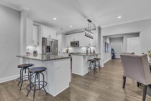 kitchen featuring white cabinets, appliances with stainless steel finishes, a peninsula, a kitchen bar, and pendant lighting