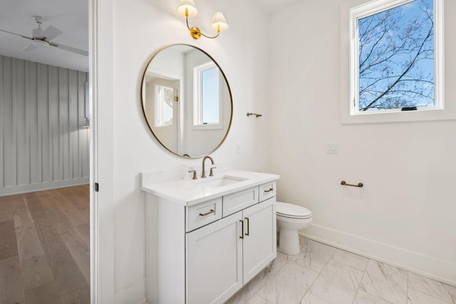 bathroom featuring marble finish floor, toilet, a ceiling fan, vanity, and baseboards