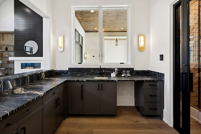 bathroom featuring wood finished floors, a glass covered fireplace, a sink, and wood ceiling